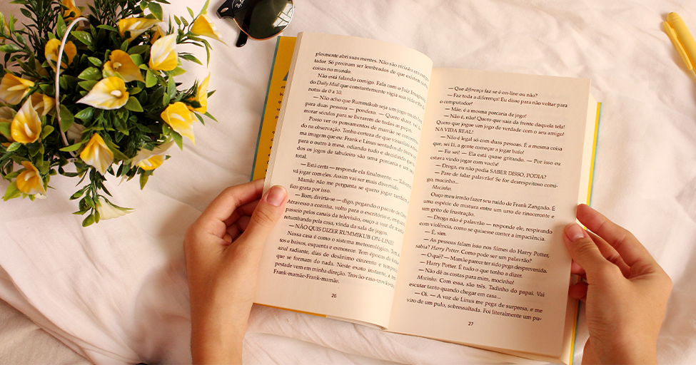 hands opening a book with flowers nearby