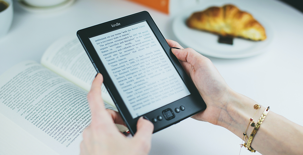 hands holding an e-book over a physical book