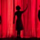 Three dark silhouettes of people in front of a red curtain