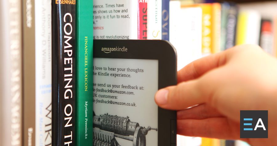 A hand pulling a Kindle ereader out of a shelf of books