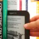 A hand pulling a Kindle ereader out of a shelf of books