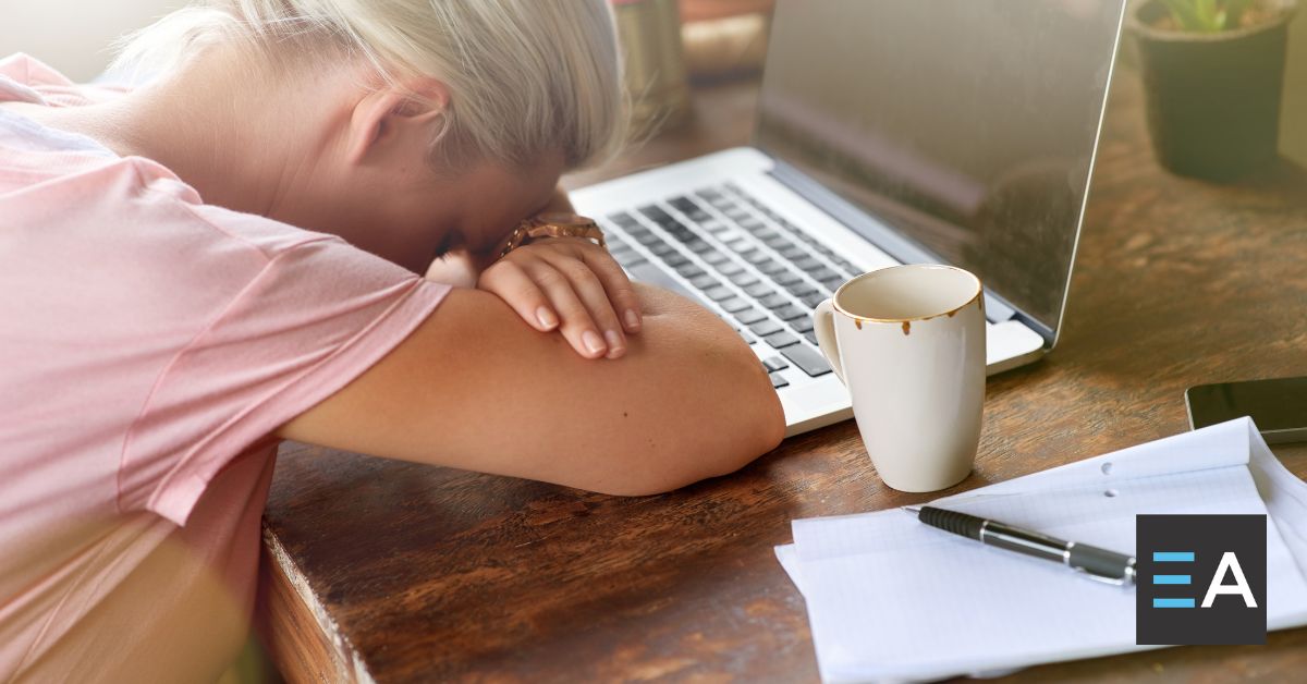 A person with their head resting on their arms in front of a laptop