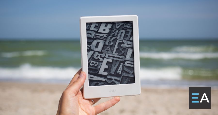 A person at the beach holding up an e-reader displaying typography tiles 