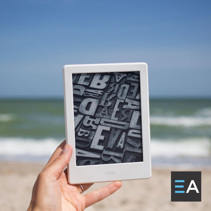 A person at the beach holding up an e-reader displaying typography tiles