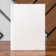 A blank white hardcover book set upright on a wooden table
