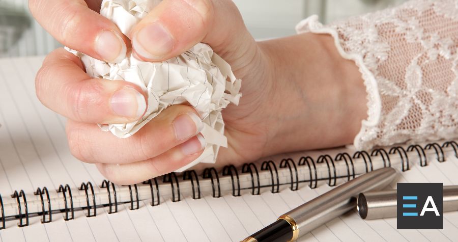 A person crumpling a piece of paper next to a notebook and pen