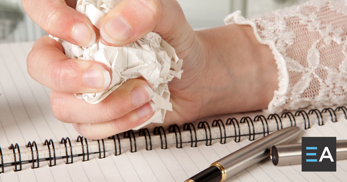 A person crumpling a piece of paper next to a notebook and pen
