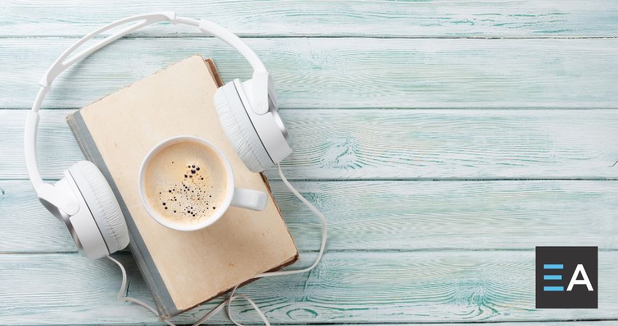 Over-the-ear headphones placed around a beige book with a cup of coffee on it
