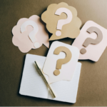 Thought and speech bubbles with questions marks on them on top of an empty notebook