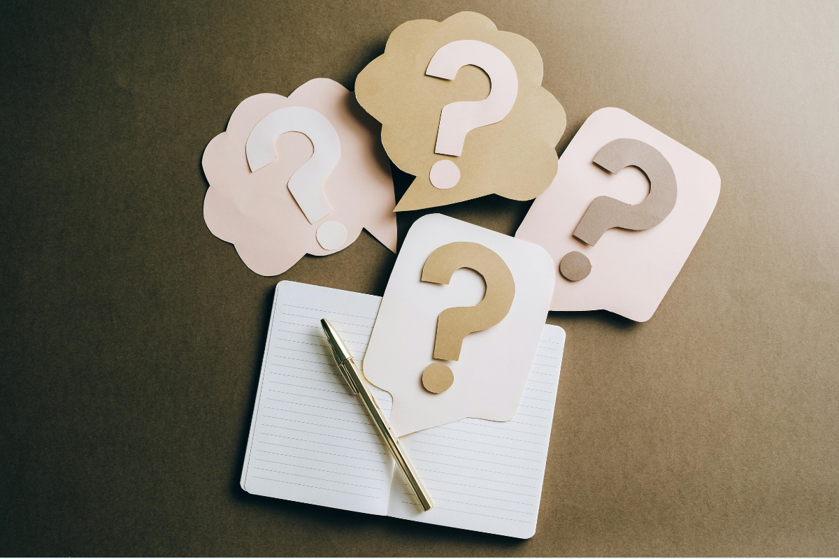 Thought and speech bubbles with questions marks on them on top of an empty notebook
