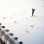 A tiny person on a notebook analyzes several different paths