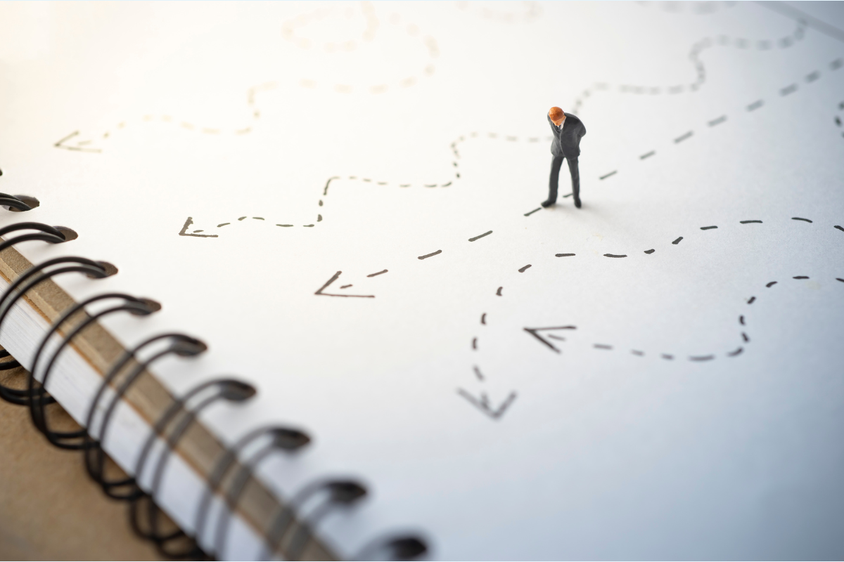 A tiny person on a notebook analyzes several different paths