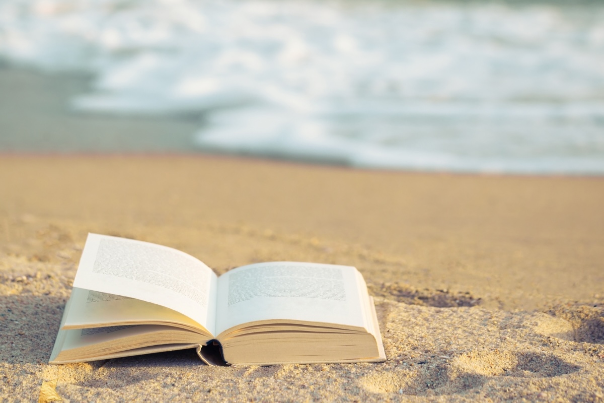 A book lies open on a sandy beach