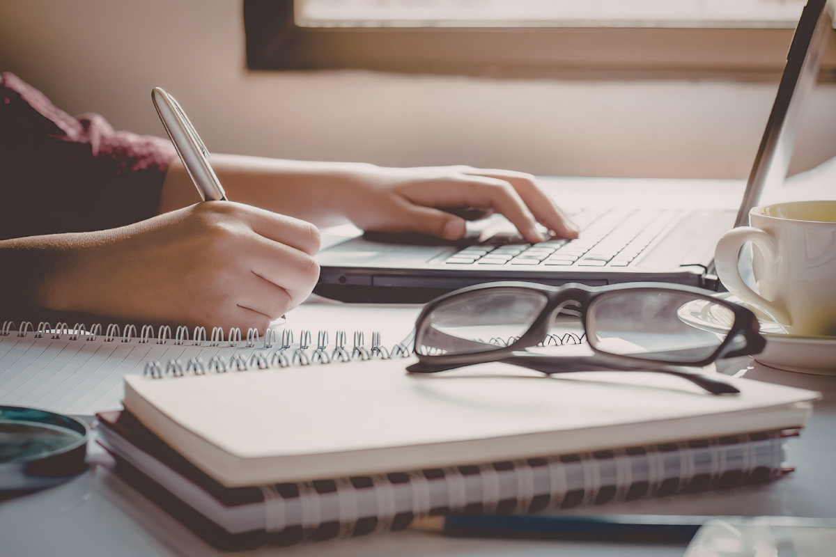 A writer uses a pen and a laptop