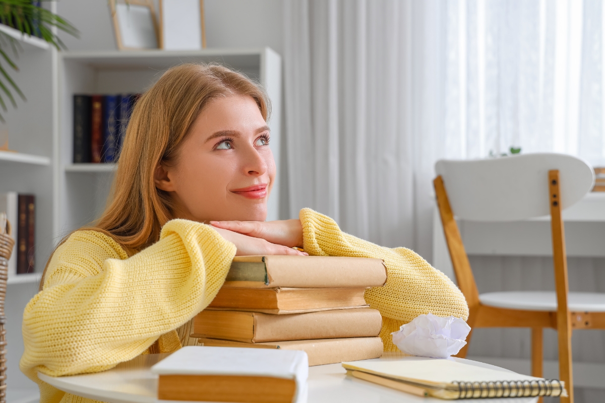 An author resting on a stack of books considers marketing strategies.