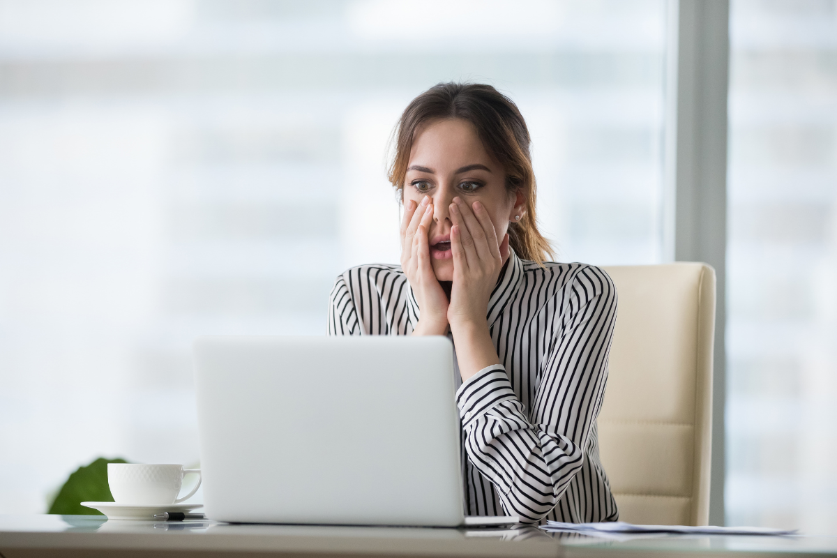 A person looking at a laptop with their hands on their face in a shocked expression