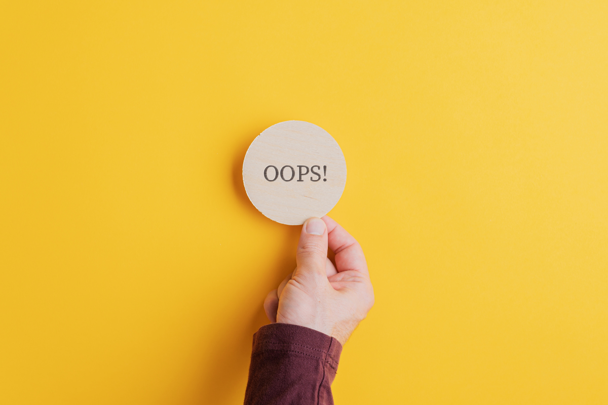 A hand holding a wooden circle with the word oops written on it