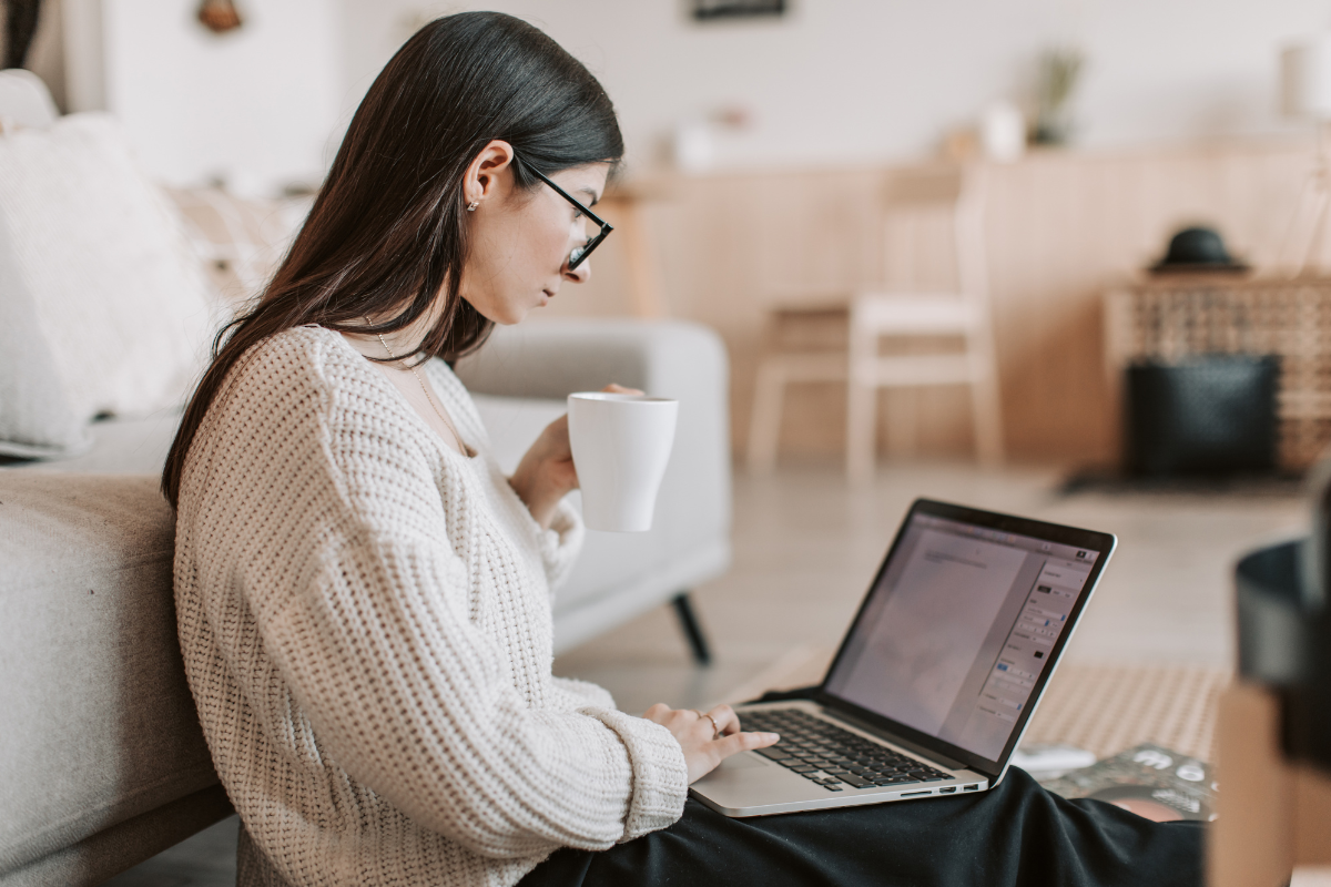 An author drinking from a mug works on a laptop