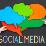 Two people hold colorful cutouts of speech bubbles above the words social media