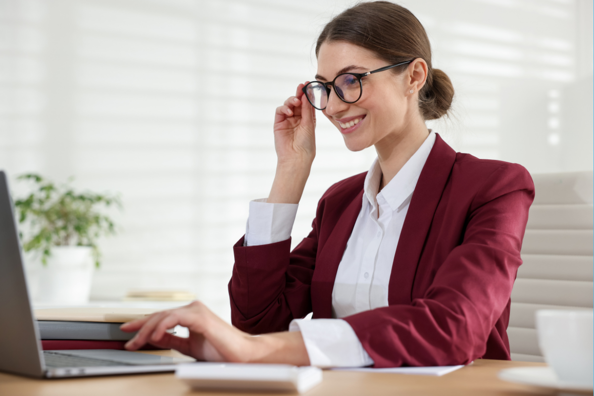 A smiling writer adjusts their glasses while working on a laptop