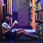 A person reads a book in an aisle of book shelves