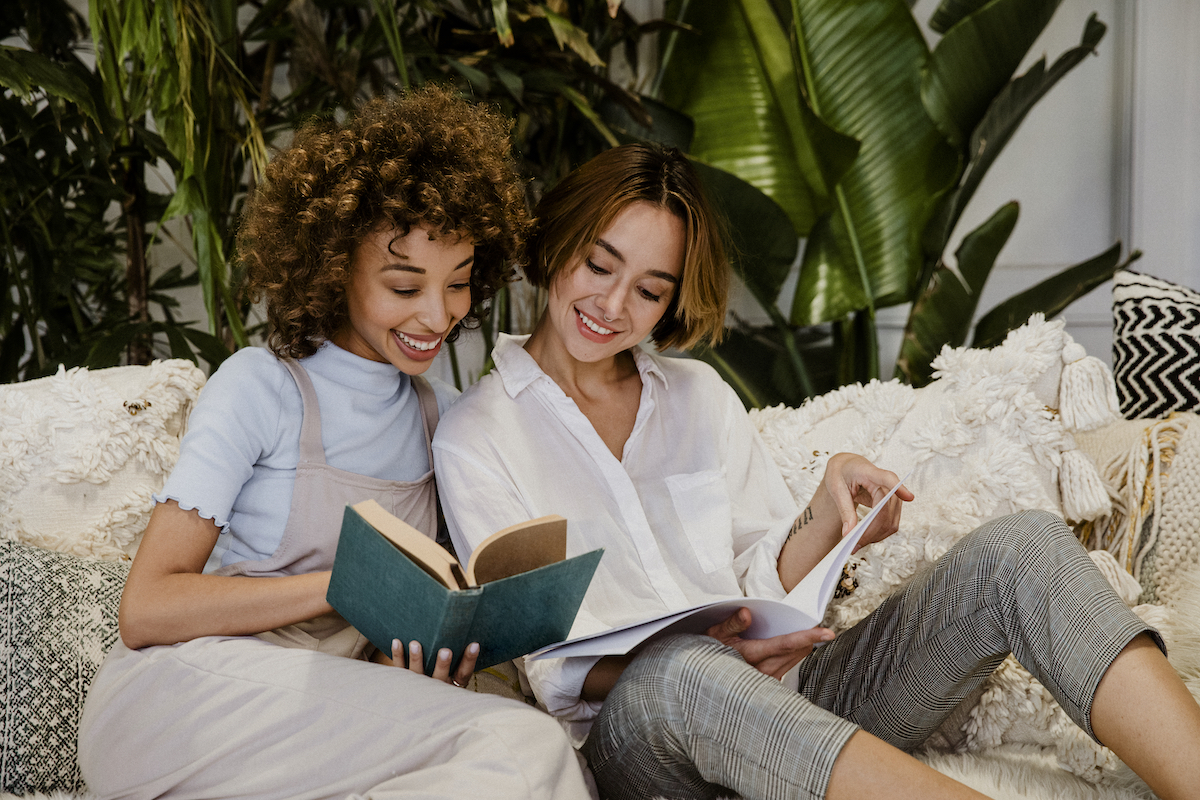 Cheerful lesbian couple reading books on a couch