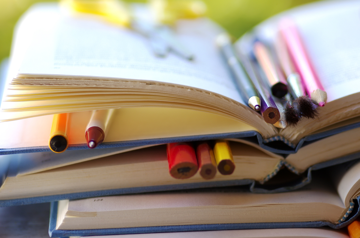 A stack of books with pens, pencils, and brushes between the pages