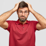 Stressed person keeps hands on head, frowns