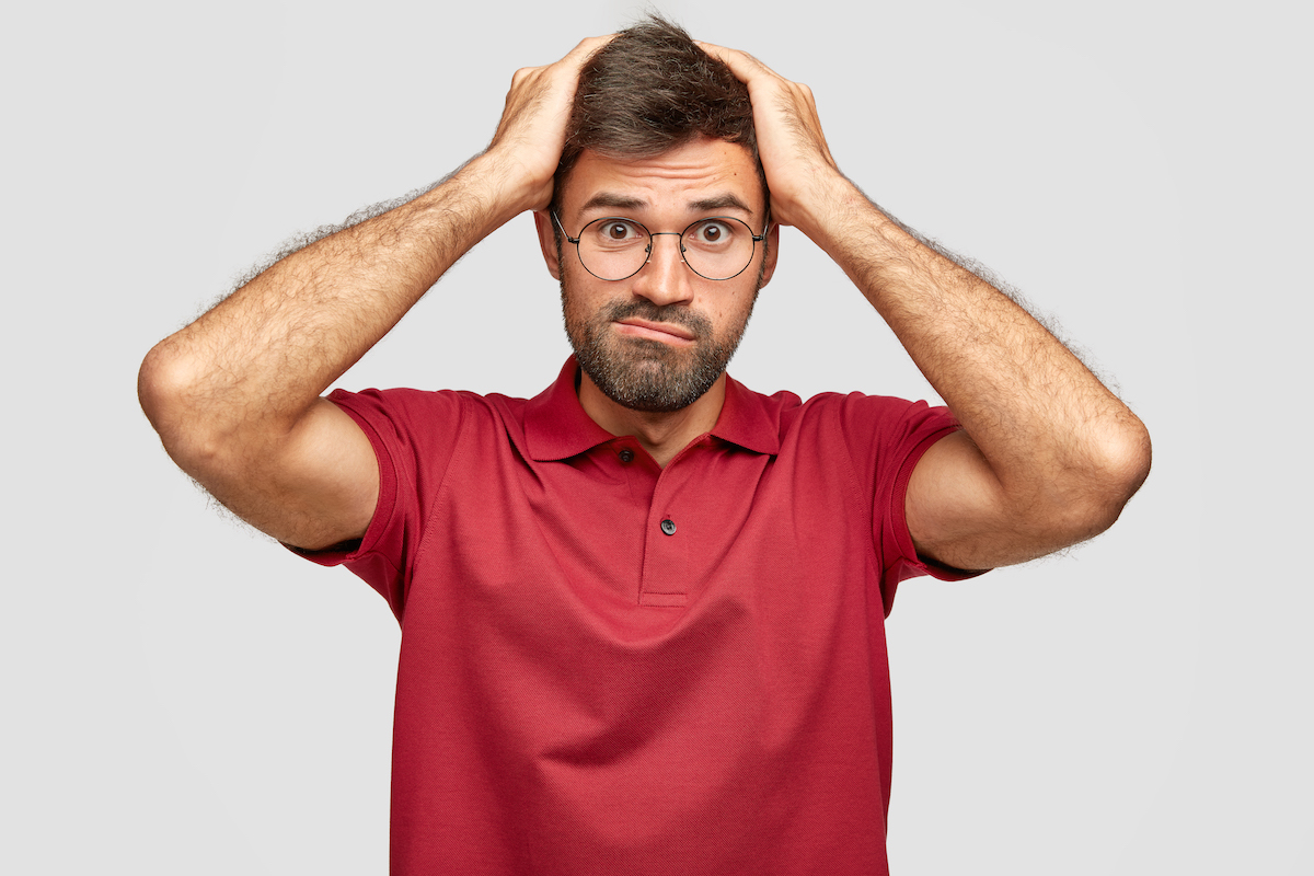 Stressed person keeps hands on head, frowns