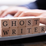 Wooden blocks that spell out ghostwriter in front of a person using a laptop