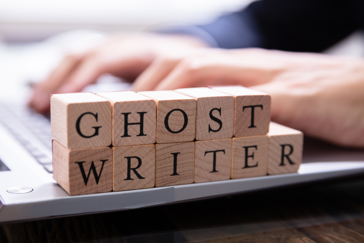 Wooden blocks that spell out ghostwriter in front of a person using a laptop