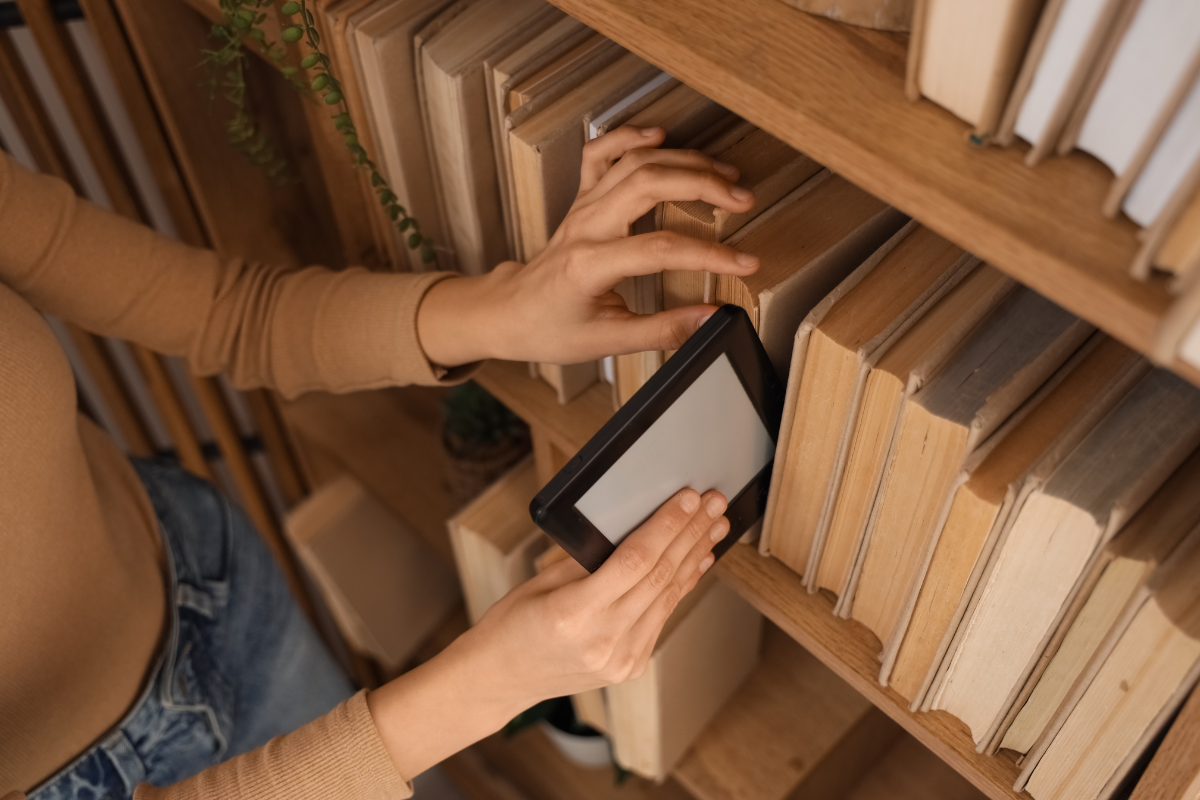 A person pulls an ereader out of a shelf of print books