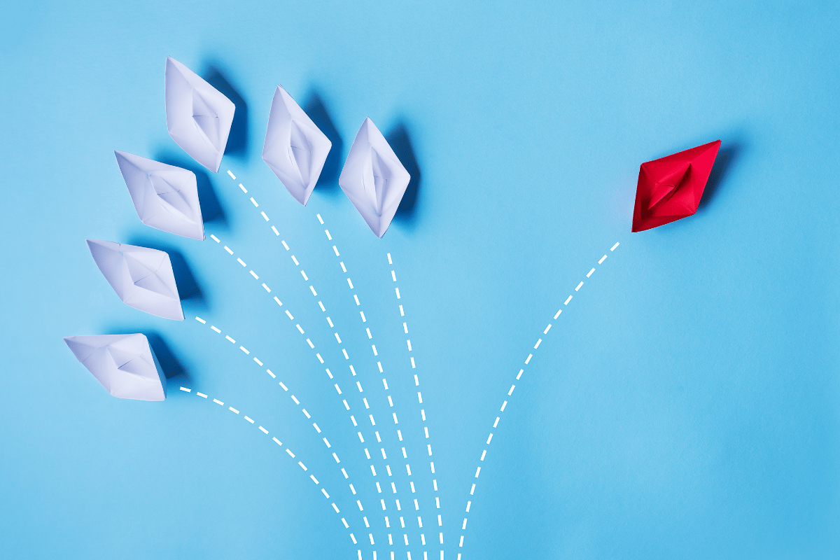 A group of white paper boats and a single red paper boat going in different directions