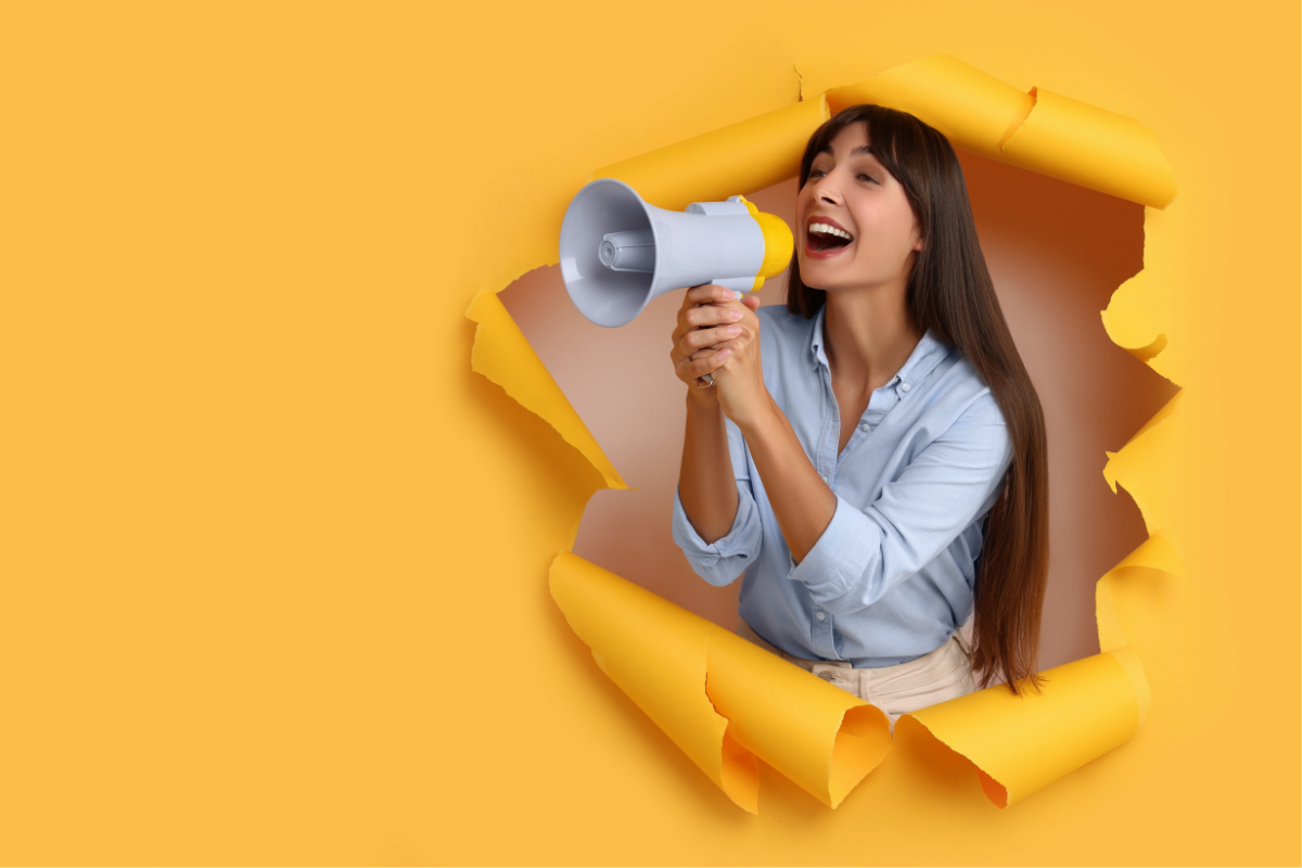 A person with a megaphone tears through a yellow paper foreground