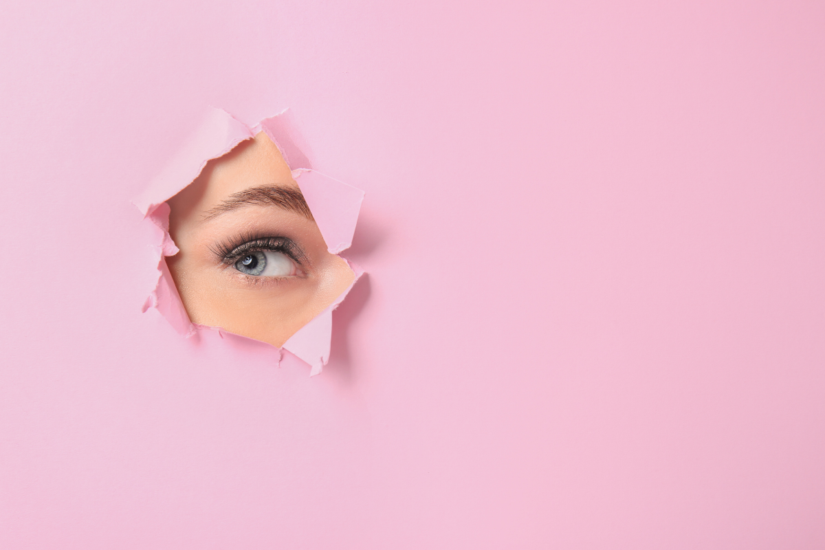 A person's eye visible through a pink paper foreground