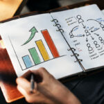 A person makes notes in a binder displaying marketing graphs