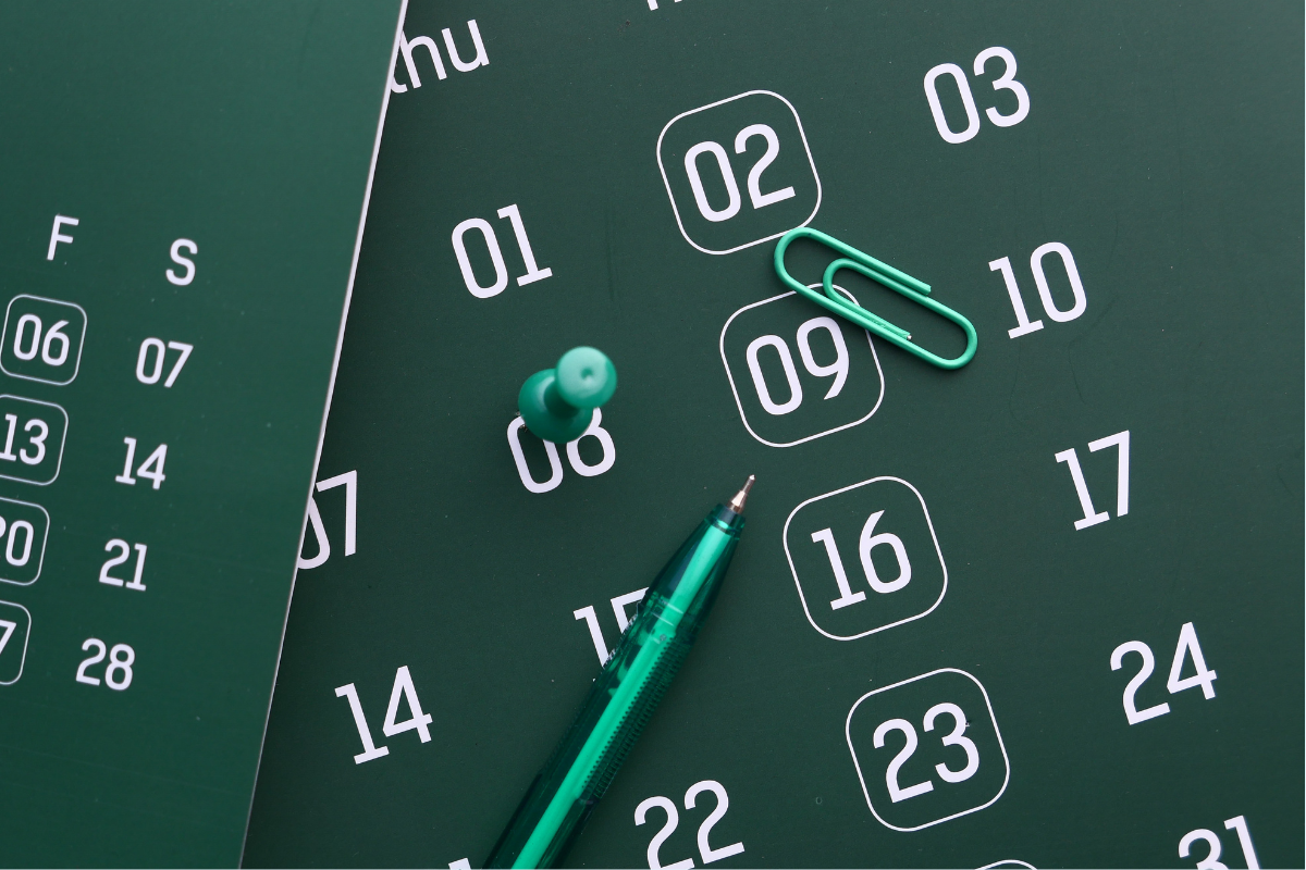 A paperclip and thumb tack on top of a monthly calendar
