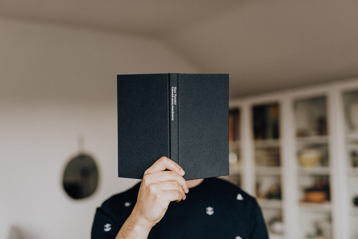 An author holds up an open book, covering their face