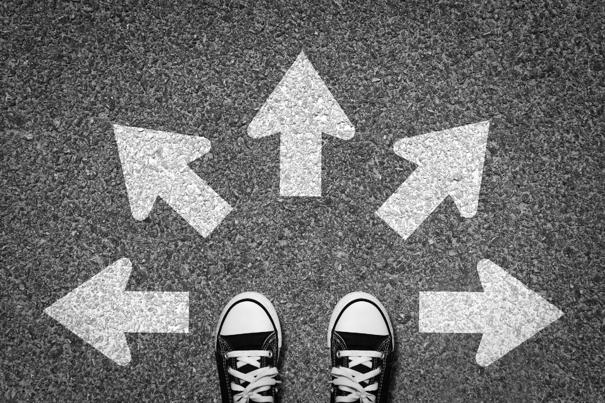 Five white arrows on asphalt point a person wearing sneakers in different directions 