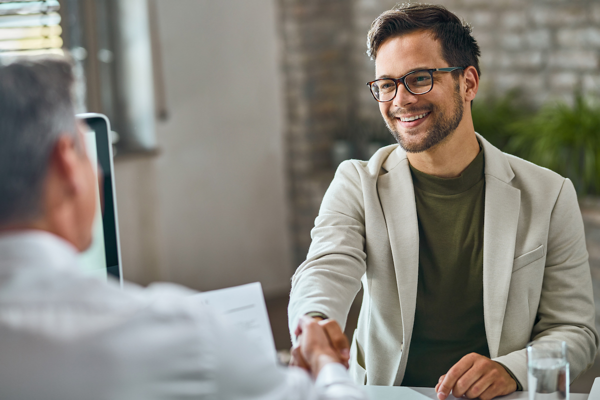 A smiling person shakes hands with someone behind a desk